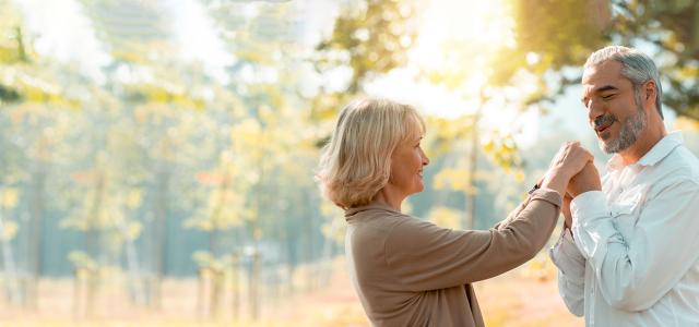 vsenior woman and man hug together and kiss on wife's hand on a fallen autumn leaves in a park